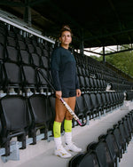 Woman standing in between black chairs wearing bright yellow compression socks. 